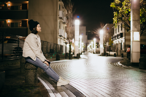 Free Woman sitting on a bench in an illuminated urban street at night, reflecting a peaceful moment. Stock Photo