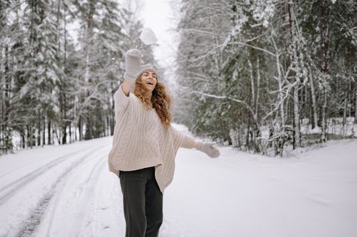 Free Woman throws a snowball in a snowy forest, expressing joy and playfulness in a winter landscape. Stock Photo