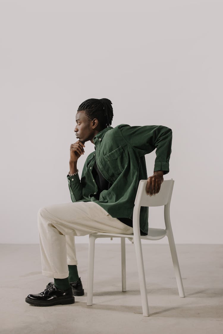 Side View Of A Man In A Green Shirt Sitting On A White Chair