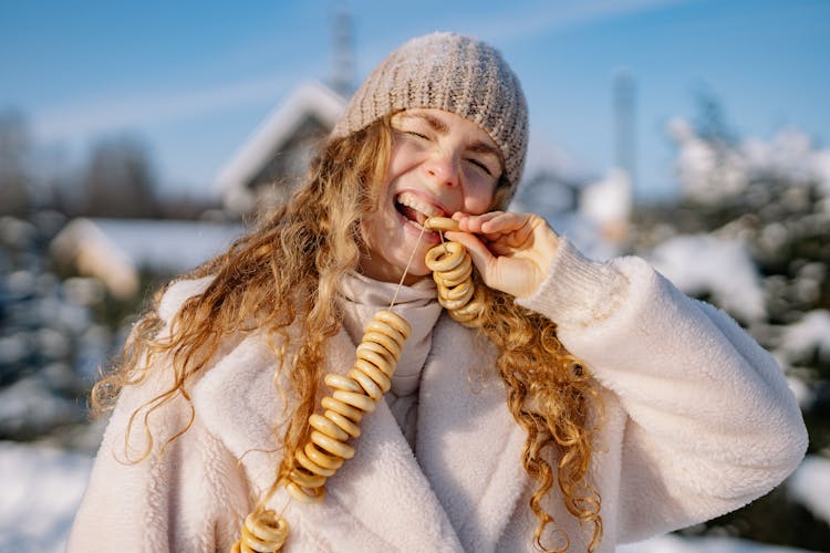 Woman In Winter Coat And Cap Eating Ring Pretzels On The String