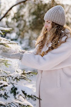A woman in winter clothing enjoys playing with snow on a tree outdoors in a serene winter wonderland.