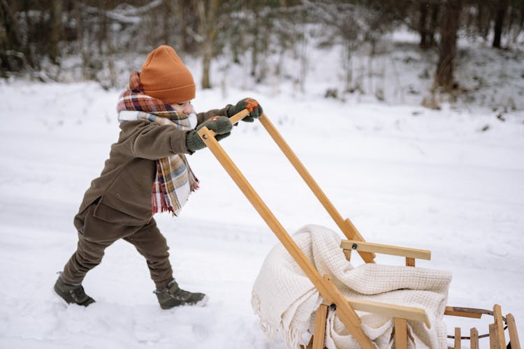 Little Child Pushing Sled In Winter 