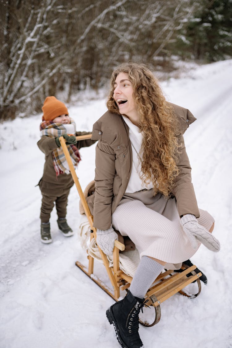 Woman In Gray Coat And A Child Playing On A Snow Covered Ground