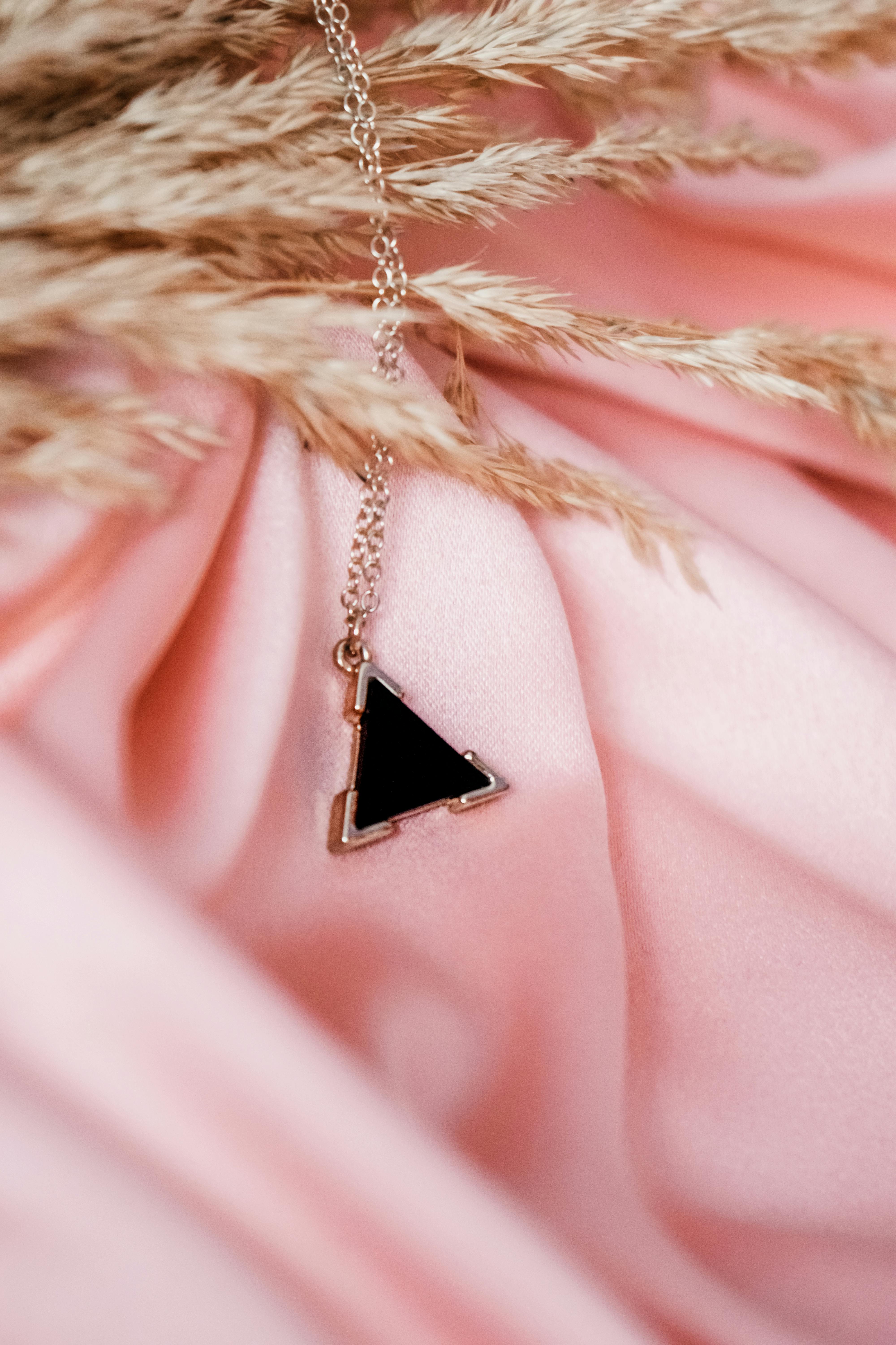 Delicate triangle pendant necklace resting on pink fabric with dried grass accents, exuding subtle elegance.