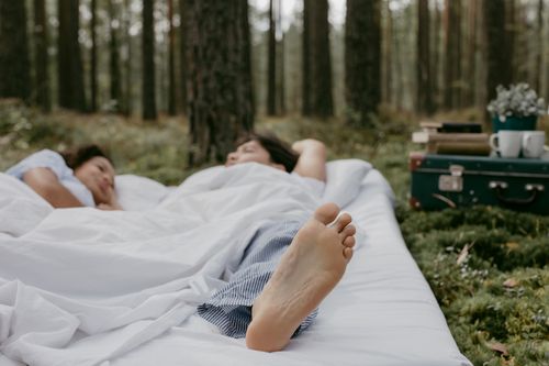 Free A couple peacefully resting on a white blanket in a forest setting, capturing tranquility and nature. Stock Photo