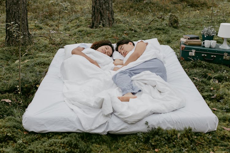 A Couple Lying Down On A Mattress Outdoors