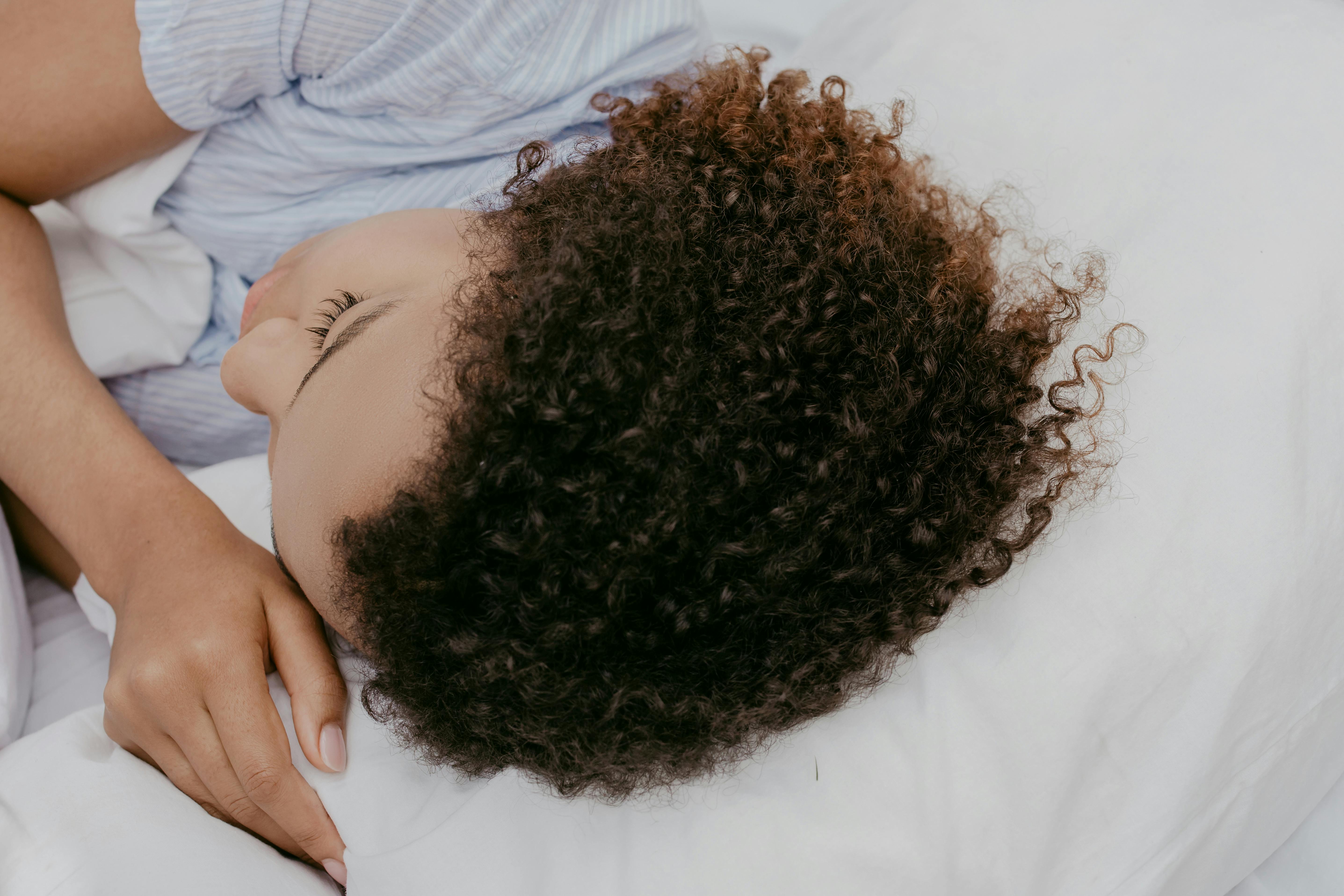 A woman resting peacefully on a pillow, showcasing natural curly hair from a close-up angle.