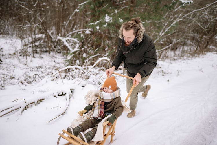 A Man Pushing A Sledge On The Snow Covered Ground With A Kid