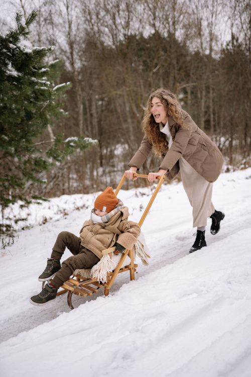 Free A joyful moment of a mother pushing her child on a sled outdoors in winter snow. Stock Photo