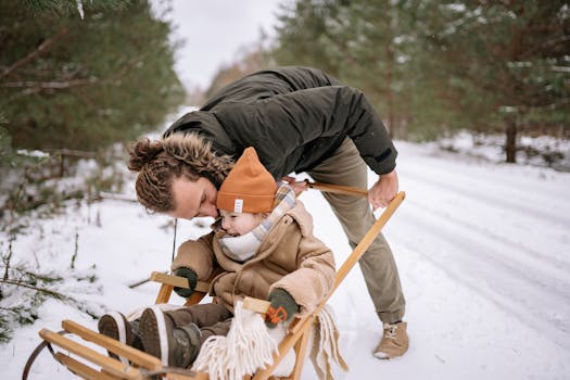 A father kissing his child on a sled in a snowy forest, capturing a joyful winter moment.