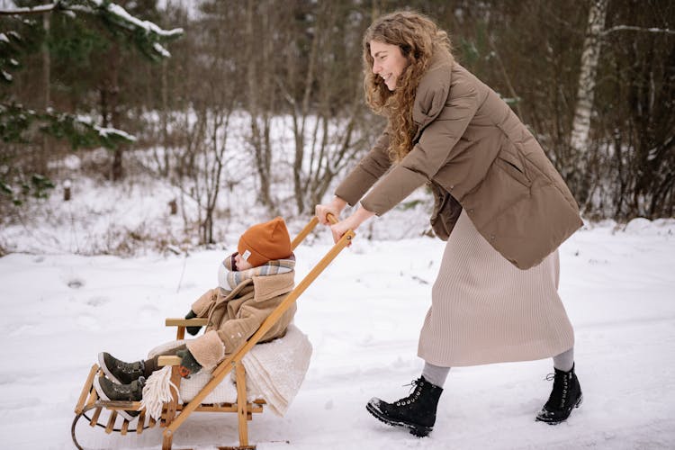 A Woman Pushing Her Child On A Wooden Sled Stroller