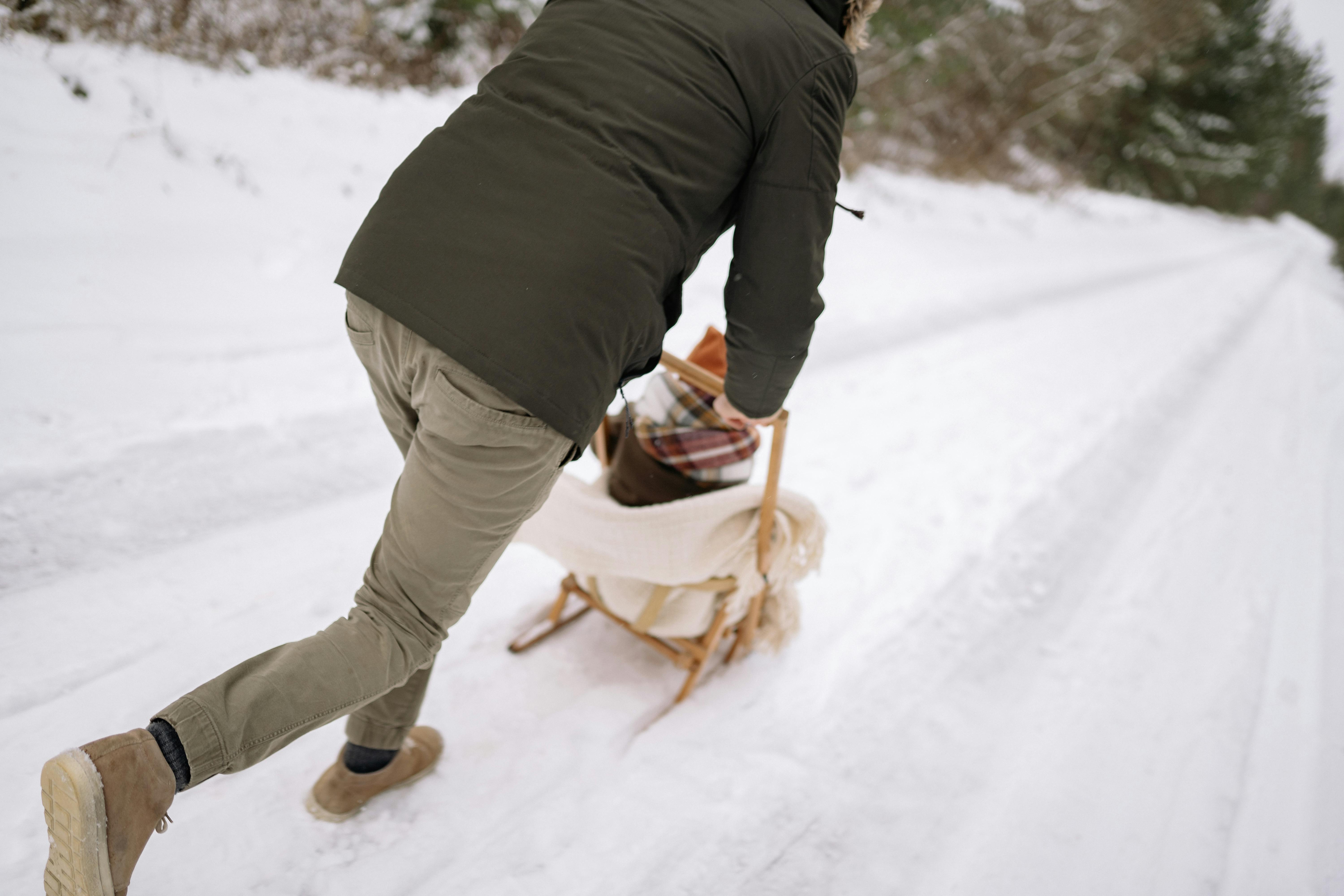 A father playfully pushes his child on a sled down a snowy path during winter.