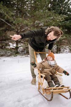 Man guiding child on a sled through a snowy forest in winter. Warm outfits.