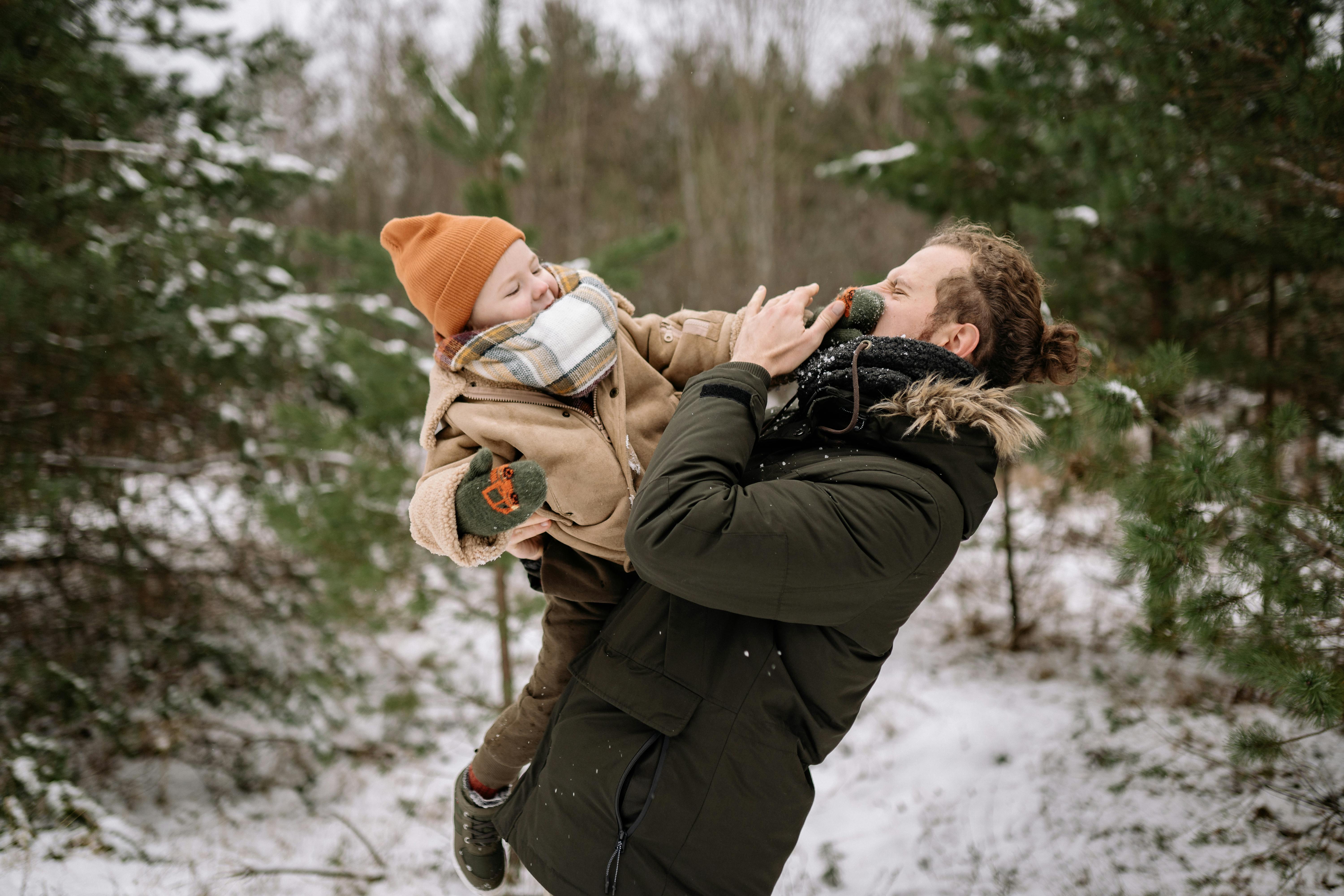 A father and son dressed warmly playing joyfully in a snowy forest setting.