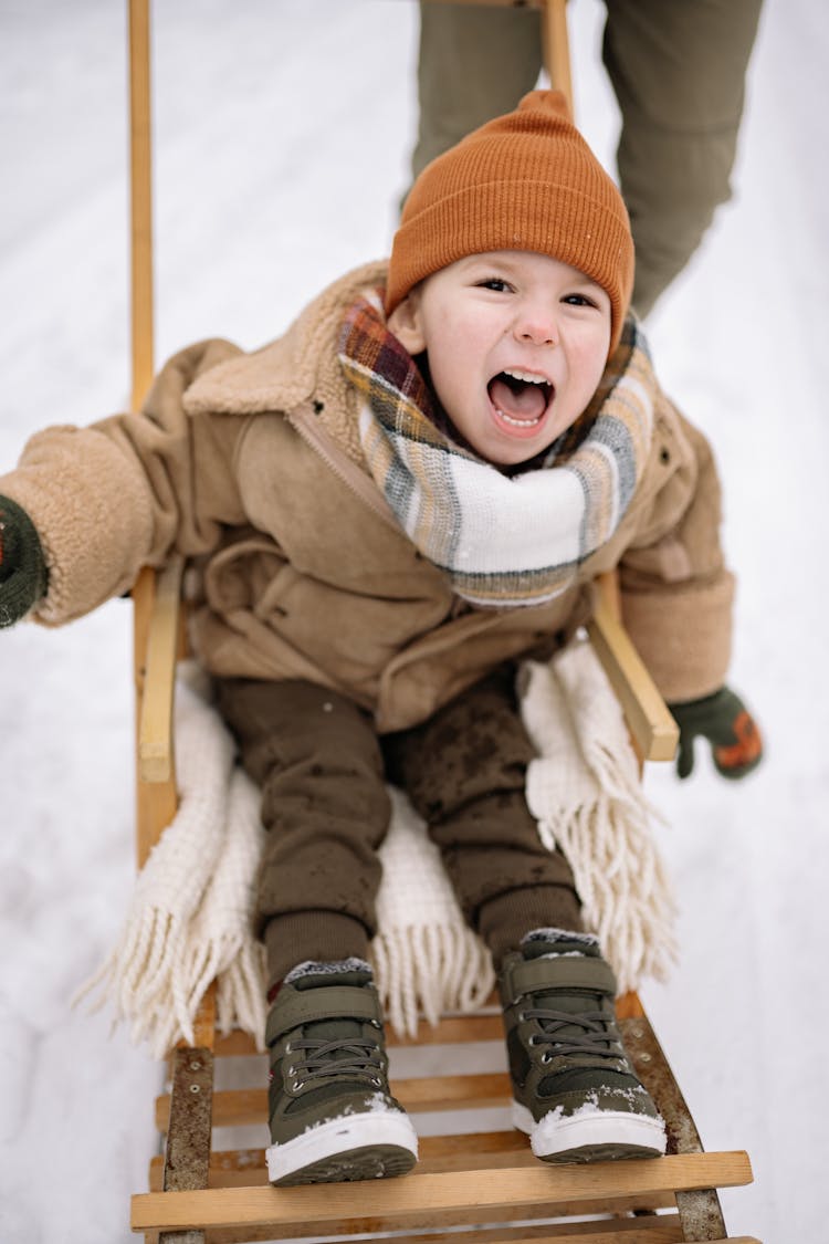 A Kid Sitting On A Sled On The Snow Cover Ground