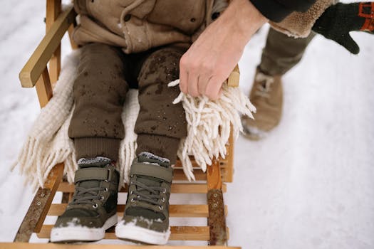 A parent helps a child on a sled in a snowy winter landscape, showcasing cozy winter fashion.