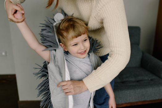 A joyful child wearing a hedgehog costume with a parent assisting indoors.