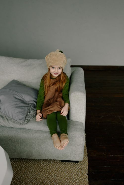 Free Adorable child in a cute costume sitting on a sofa indoors, exuding a cozy and playful atmosphere. Stock Photo