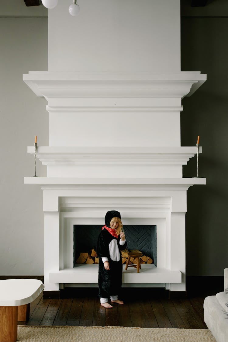 A Girl Standing By The Fireplace Wearing A Costume