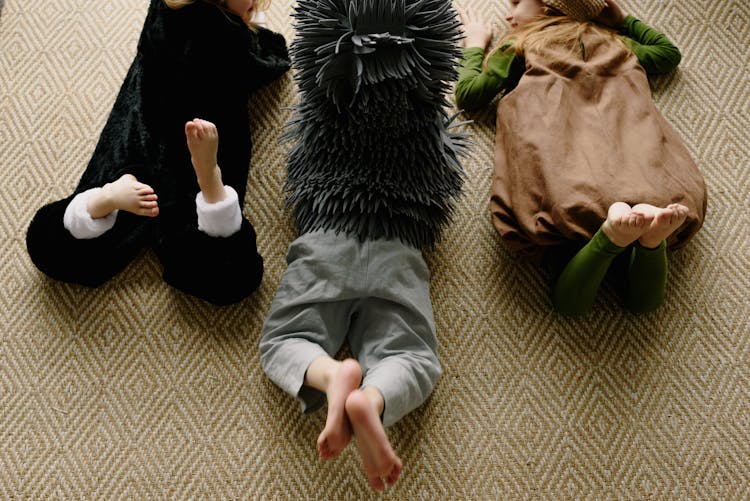 Children Lying On A Carpet Flooring Wearing Costumes