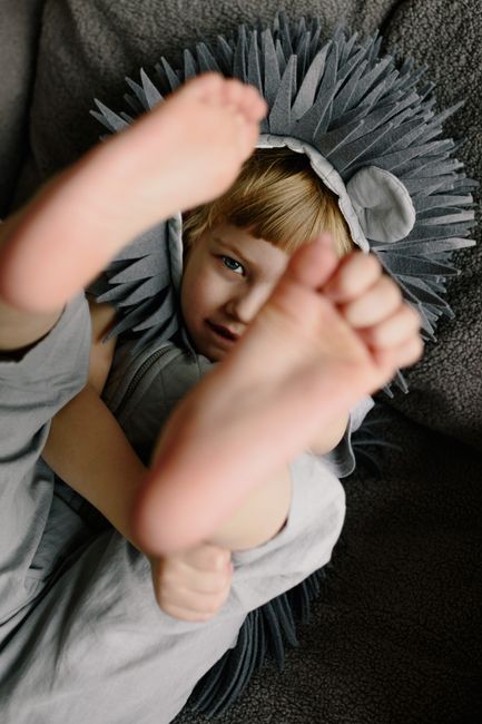 Young child playfully lying in a lion costume, showcasing bare feet indoors.