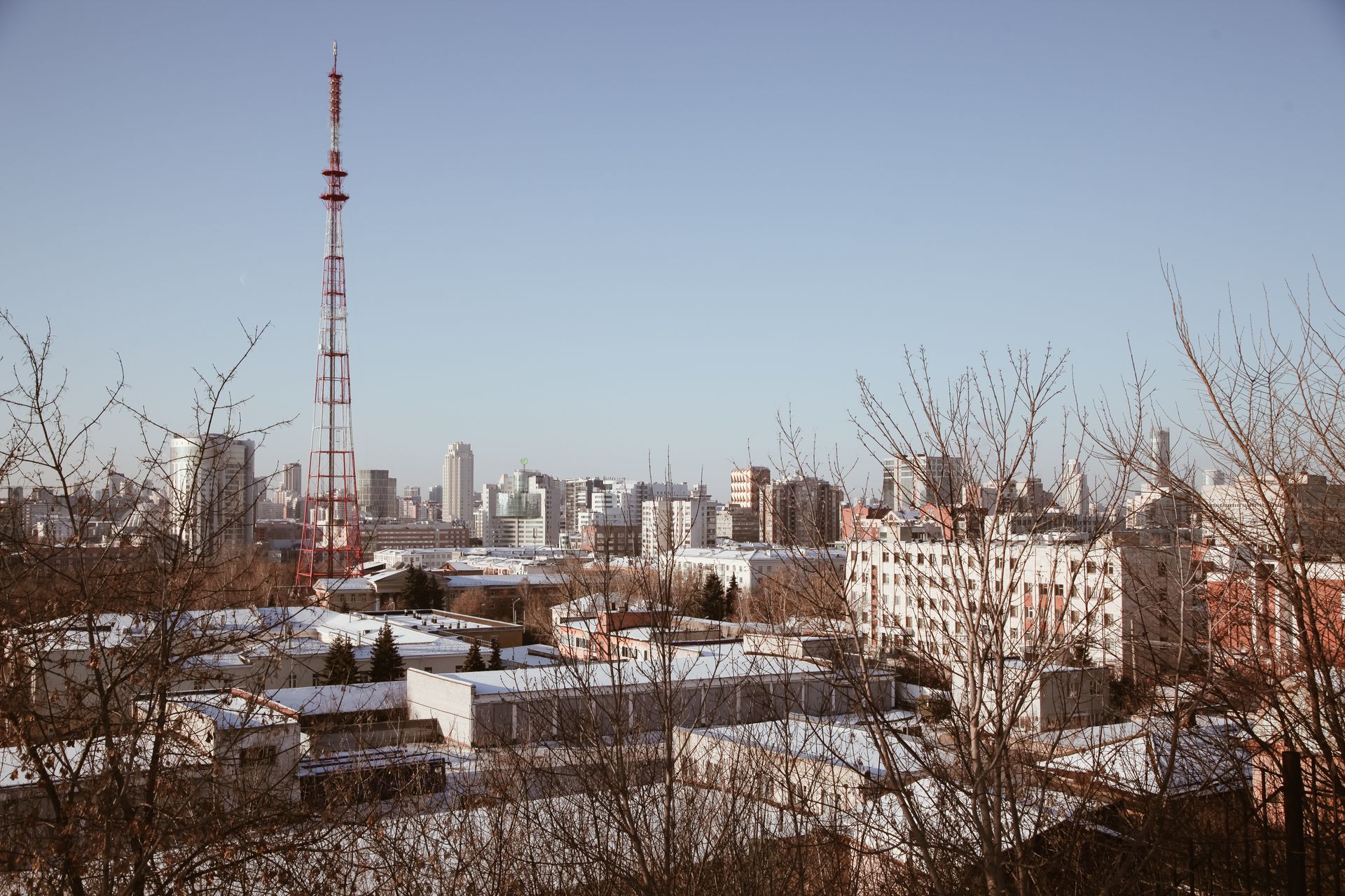 Snow-covered cityscape featuring a red radio tower and modern buildings in winter.