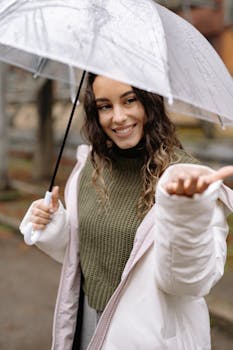 Young woman enjoying the rain under an umbrella, smiling warmly.