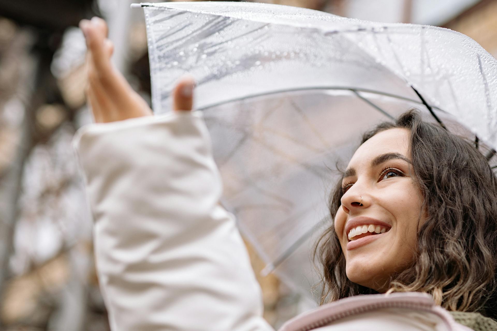 Woman smiling under a clear umbrella during a rainy day, capturing joy and nature's beauty.