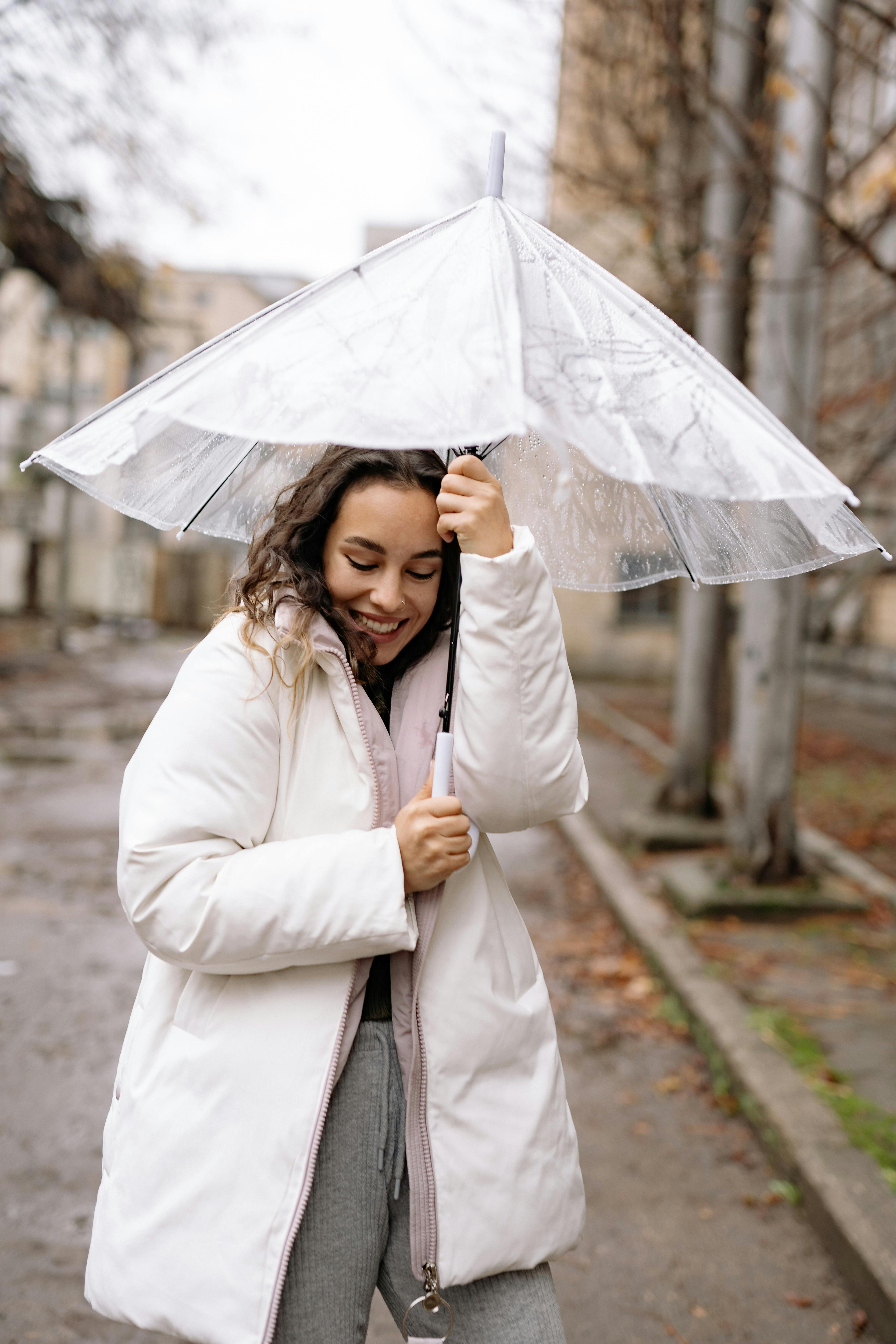 a woman in white jacket smiling while holding an umbrella