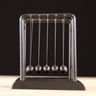 A metal Newton's cradle resting on a wooden surface against a dark background.
