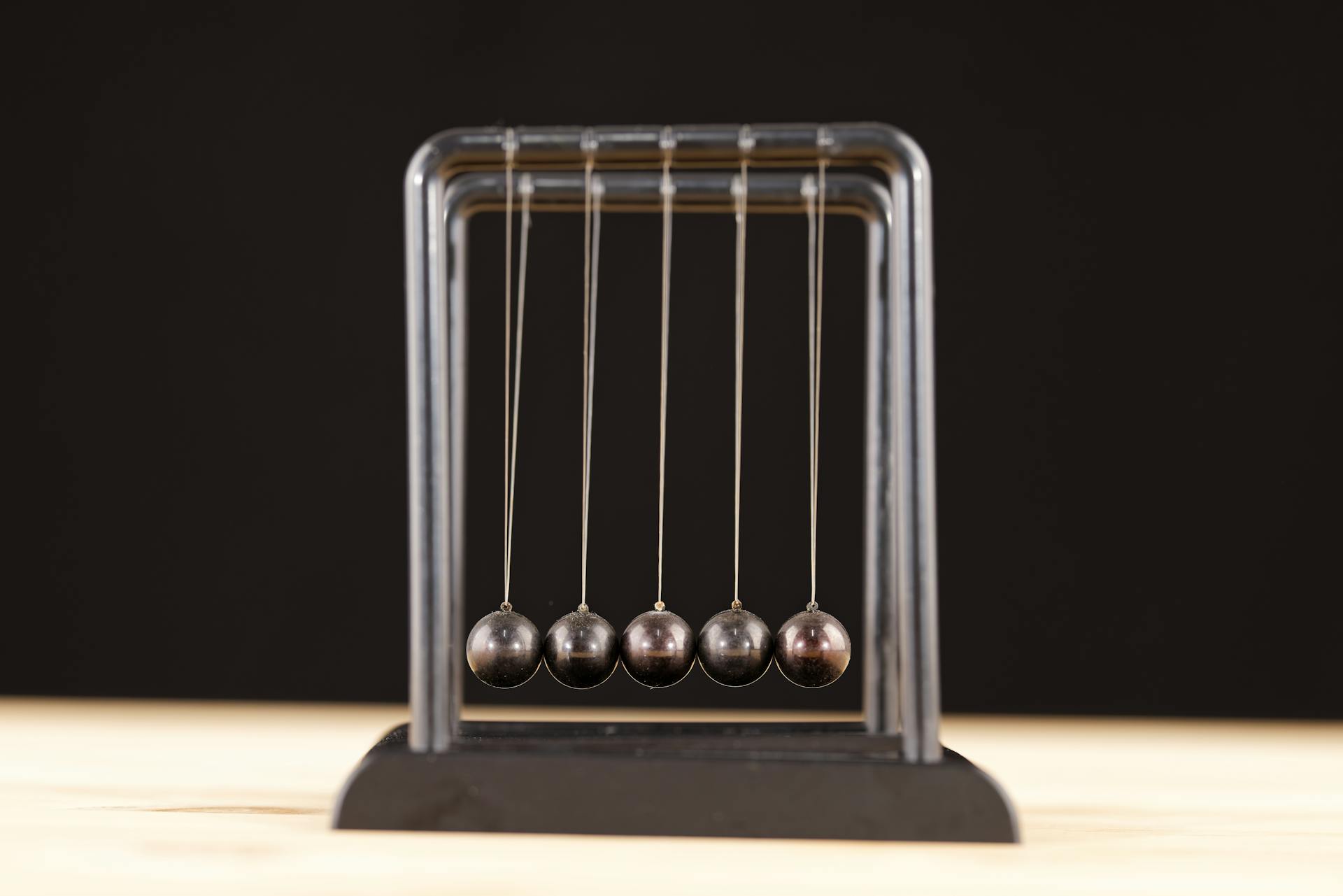 Close-up of a Newton's Cradle resting on a wooden surface against a dark background.