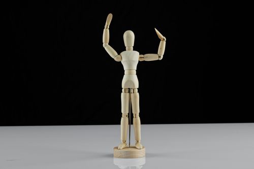 Free Wooden artist mannequin standing with arms raised on a black background, ideal for art and craft projects. Stock Photo