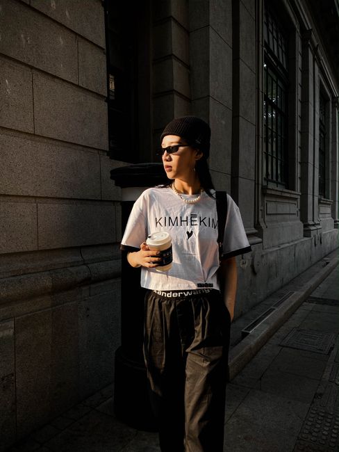 Fashionable woman walking on city street with coffee at sunset.