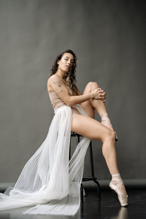 Free Studio Shoot of a Ballerina Posing on a Chair against Gray Background Stock Photo