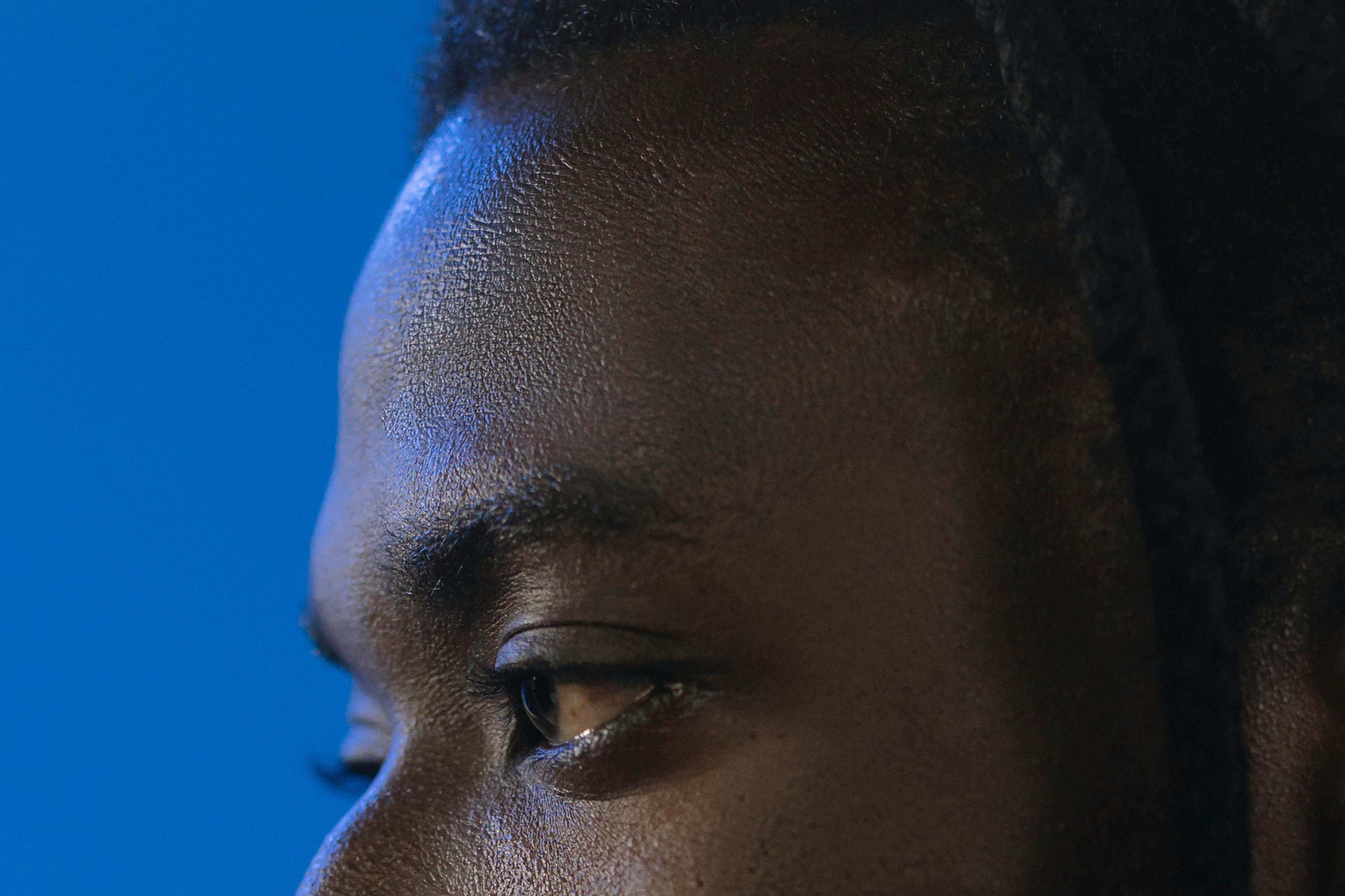 Intimate close-up portrait of a young man against a vibrant blue background, showcasing expressive eyes.