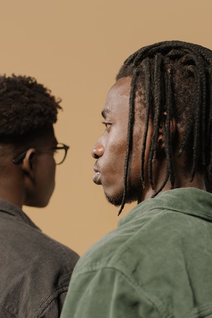 Close-up of two men in profile view highlighting braided hairstyles against a neutral background.
