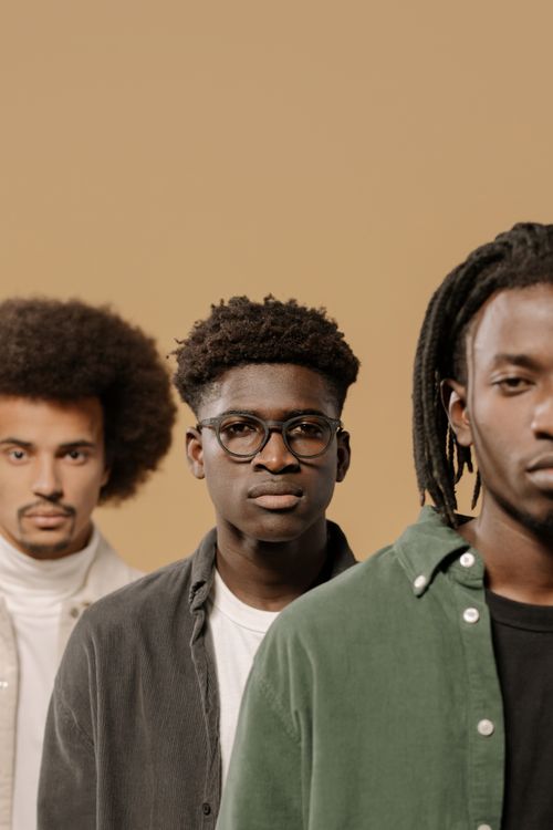 Free Portrait of three fashionable men with diverse hairstyles against a beige background. Stock Photo