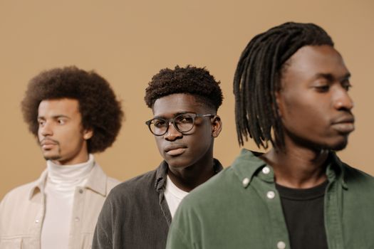 Three men posing stylishly in casual attire, looking serious. Studio shoot with a neutral background.