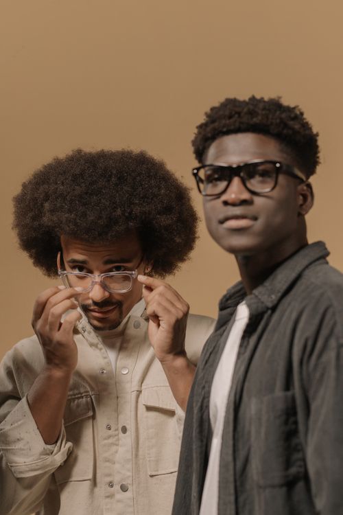Free Fashion-forward portrait of two men with glasses in a neutral setting, showcasing afro hairstyles. Stock Photo