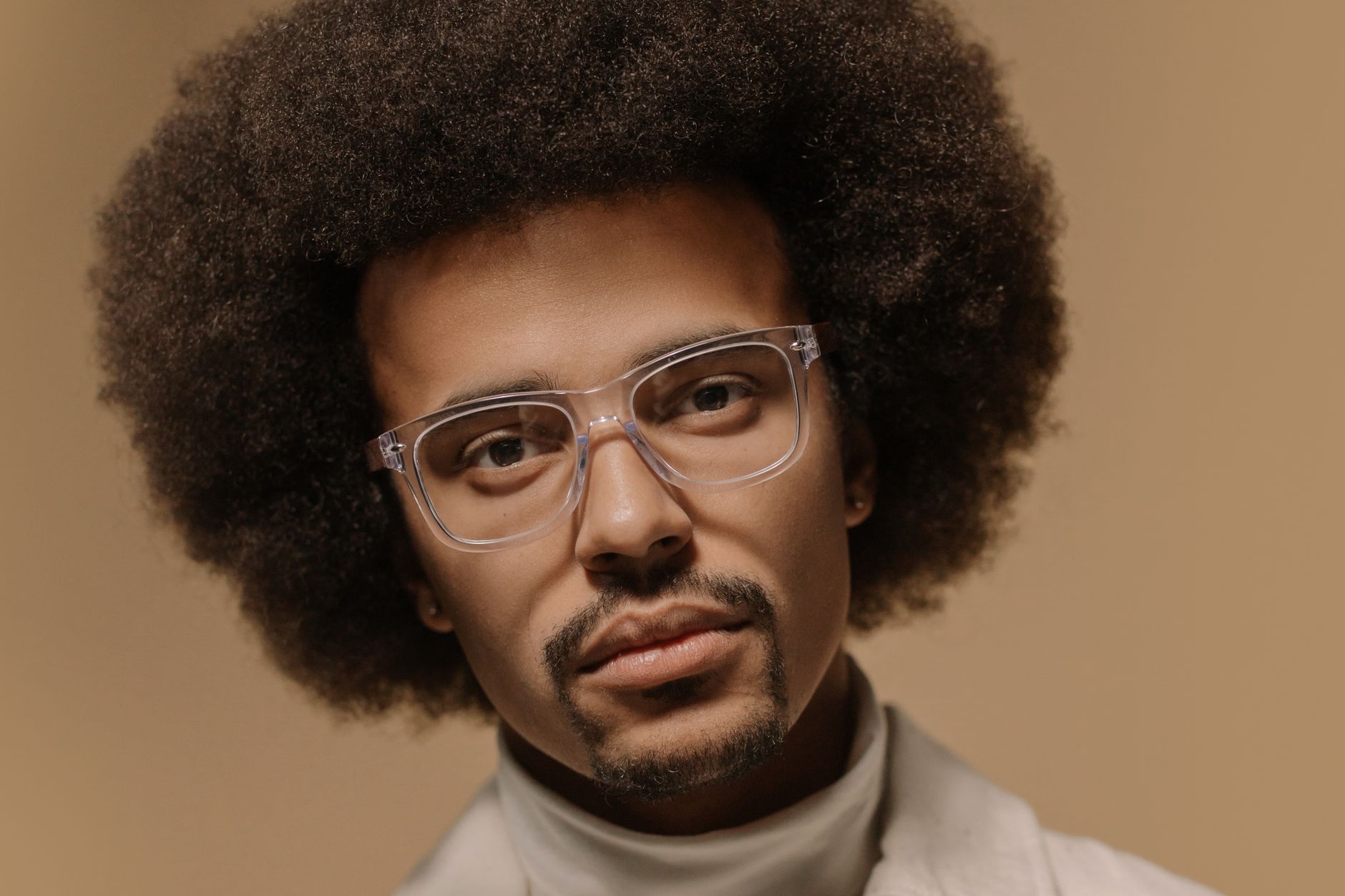 Serious-looking man with an afro and eyeglasses on a beige neutral background.