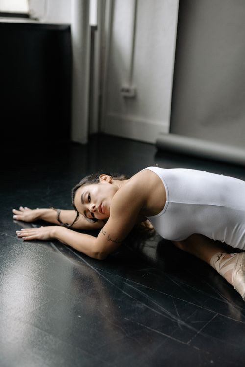 Free A ballerina in a white leotard gracefully stretches on a polished dance studio floor. Stock Photo