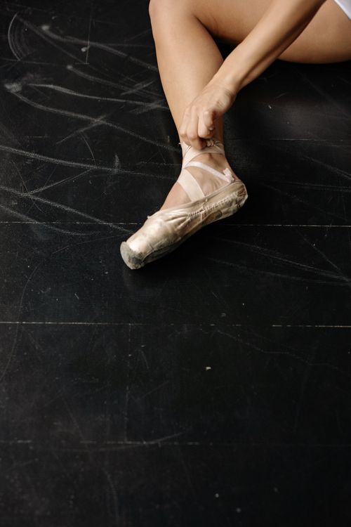 Free Close-up of a dancer’s leg as they tie their ballet shoes on a dark studio floor. Stock Photo