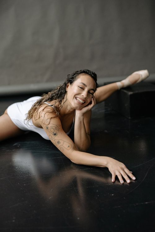 Free Ballet dancer showcasing flexibility with a joyful smile in a studio setting. Stock Photo