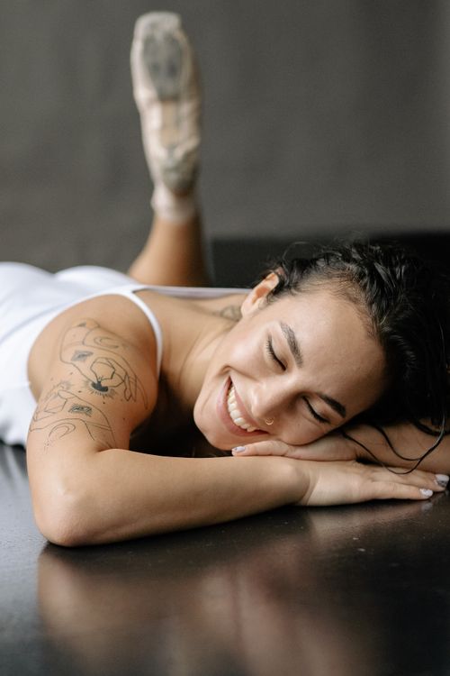 Free Happy ballerina with tattoos smiles while resting in a relaxed pose indoors. Stock Photo