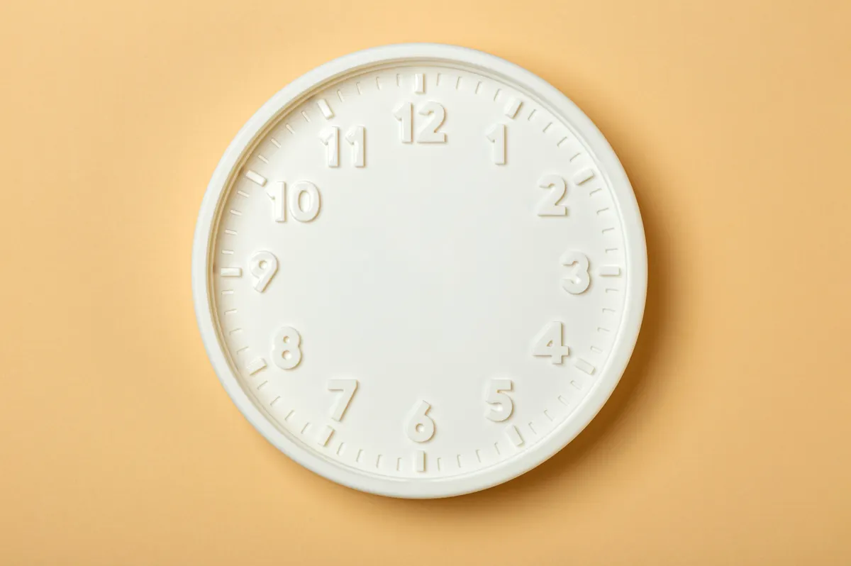 Plain white wall clock with no hands on an orange wall, a reminder that OneUp Trader positions must be flat by 3:15 PM CT