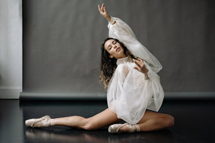 Elegant Ballerina In Ballet Shoes Sitting On Floor