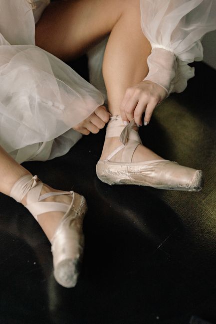 Close-up of a ballet dancer tying pointe shoes, focusing on preparation and elegance.