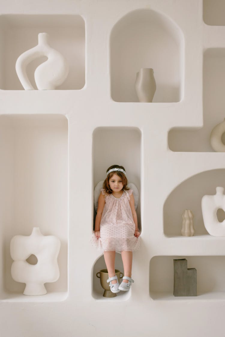 A Girl Wearing A Pink Dress And Halo Sitting On A Wall Shelf