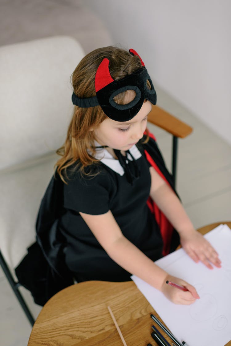 A Girl In Devil Costume Drawing On White Paper