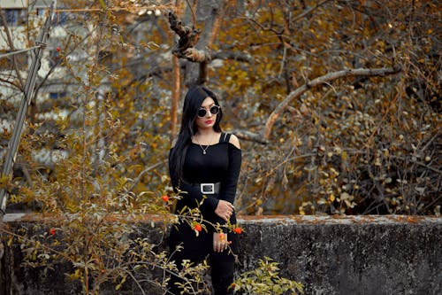 Woman in Black Dress Wearing Black Sunglasses Standing Near Concrete Wall